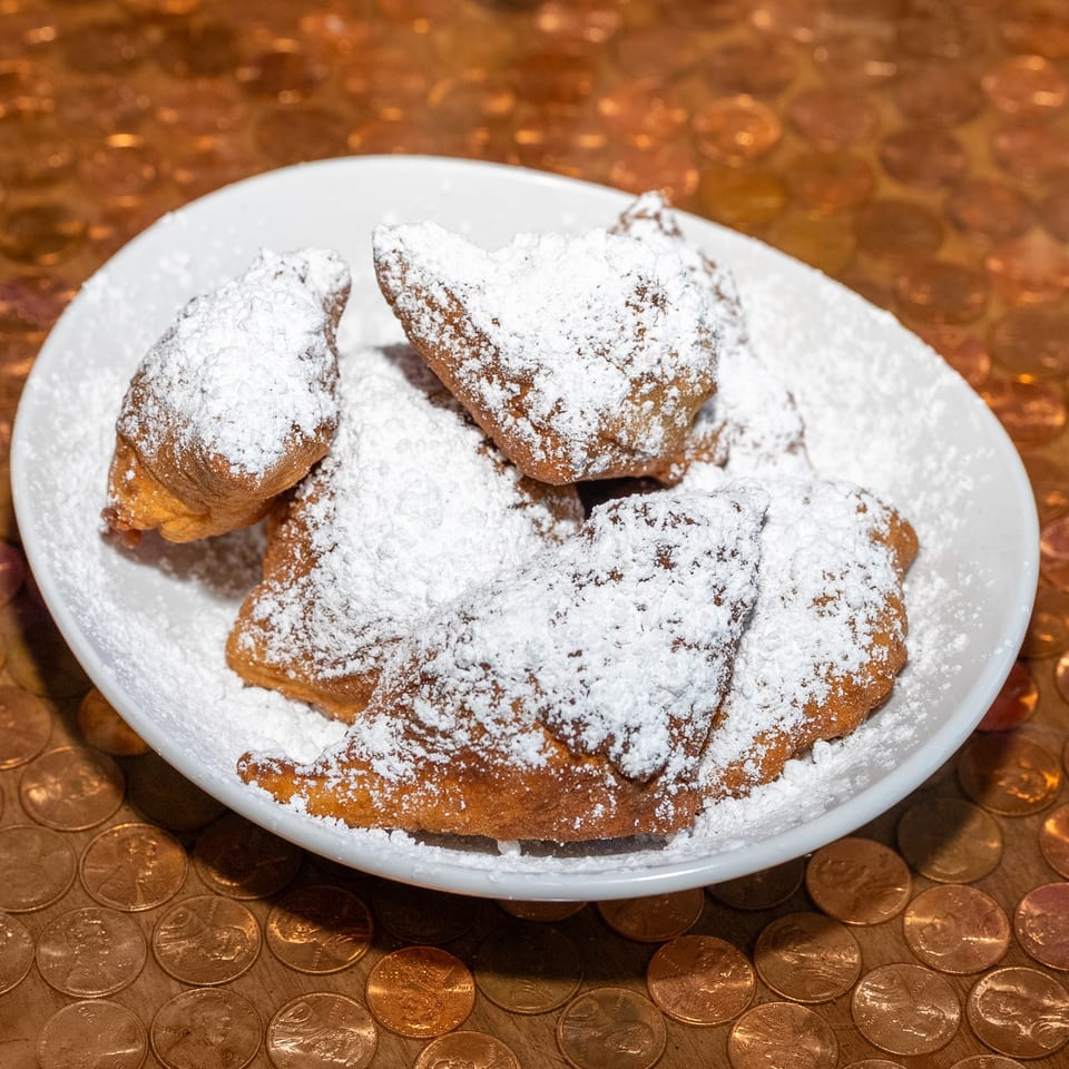 Plate of golden fried pastries generously dusted with powdered sugar on a copper penny-covered table.