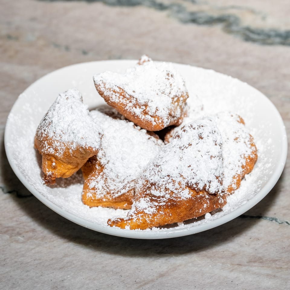 Plate of golden fried pastries generously dusted with powdered sugar on a marble tabletop.