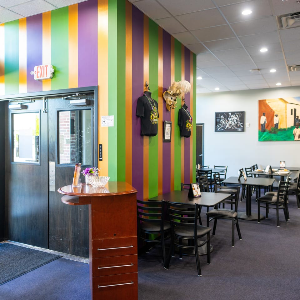 Colorful restaurant interior with striped purple, green, and orange walls, dining tables, artwork, and mannequin displays.