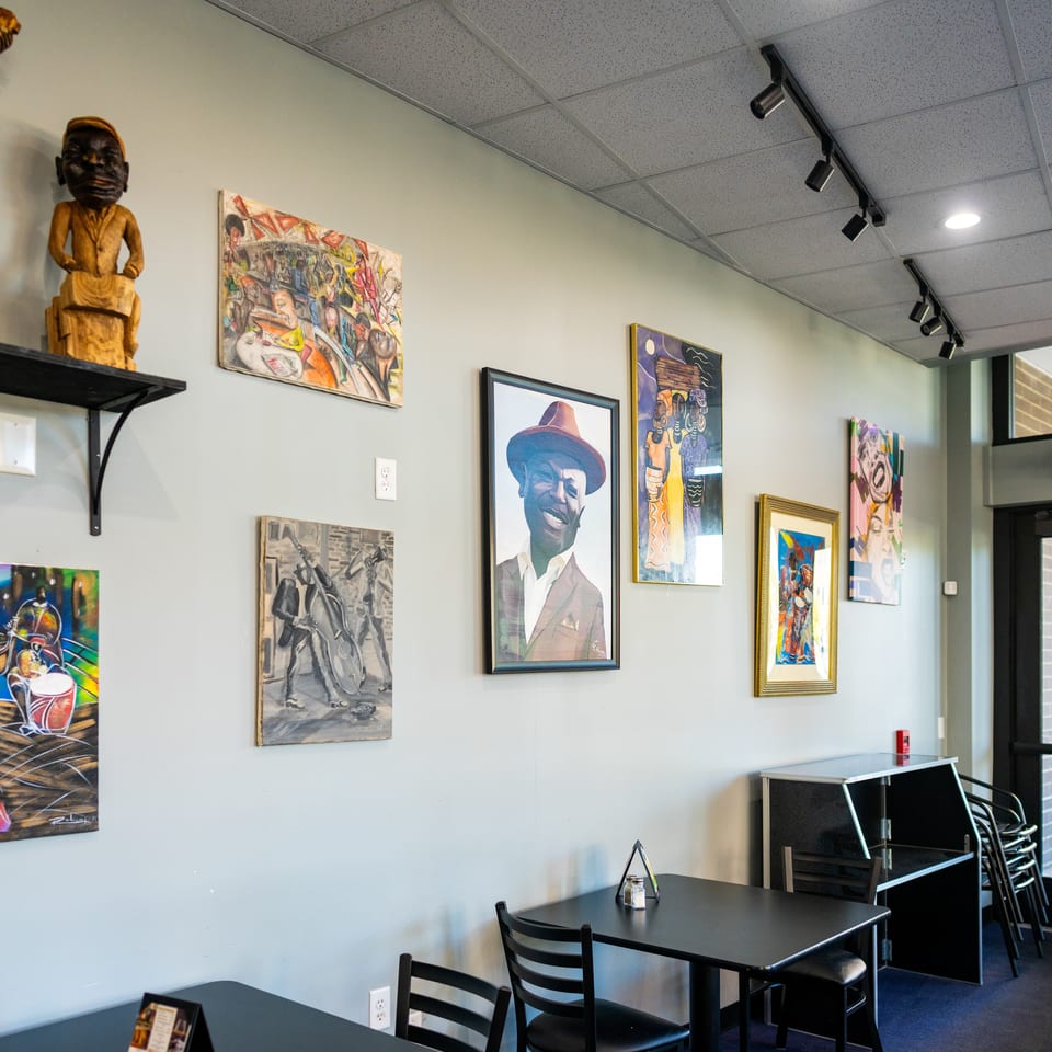 Restaurant dining area with black tables, chairs, colorful artwork, wooden sculptures, and an exit door.