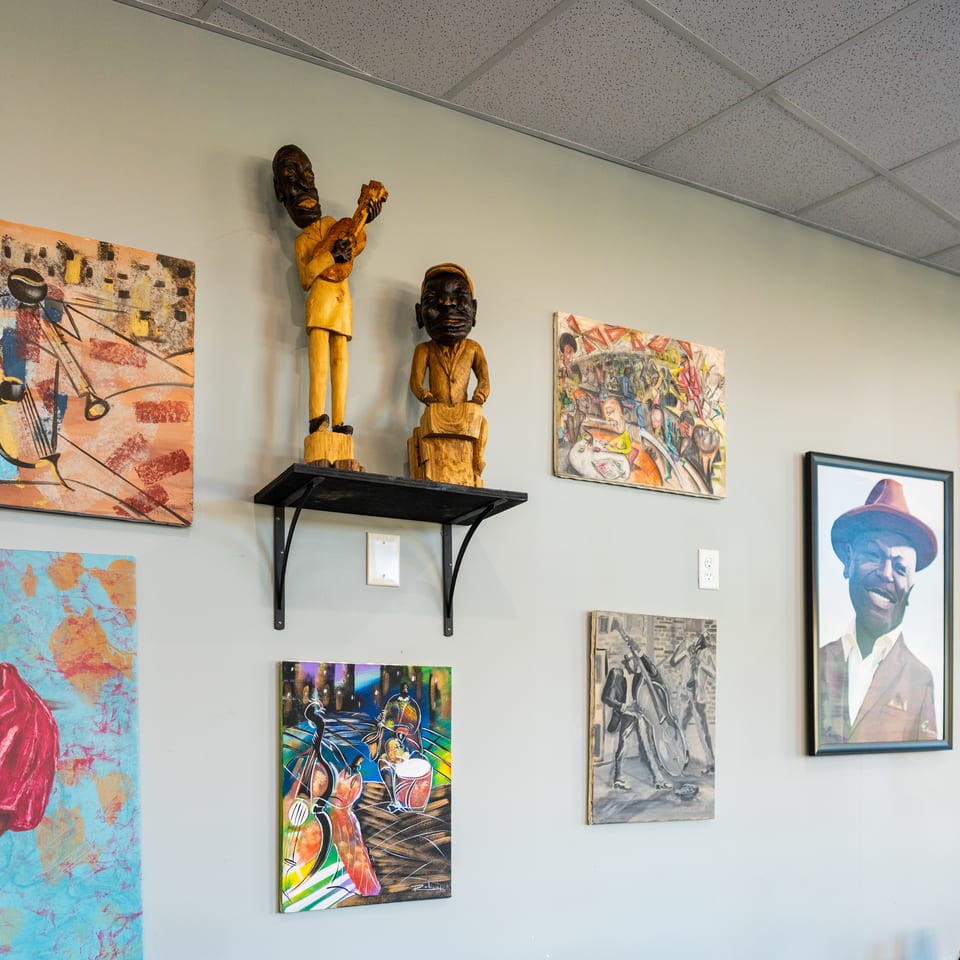 Restaurant wall displaying colorful artwork and two carved wooden figures on a shelf.