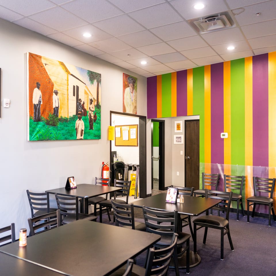 Bright restaurant dining room with black tables, chairs, colorful striped walls, and vibrant artwork.