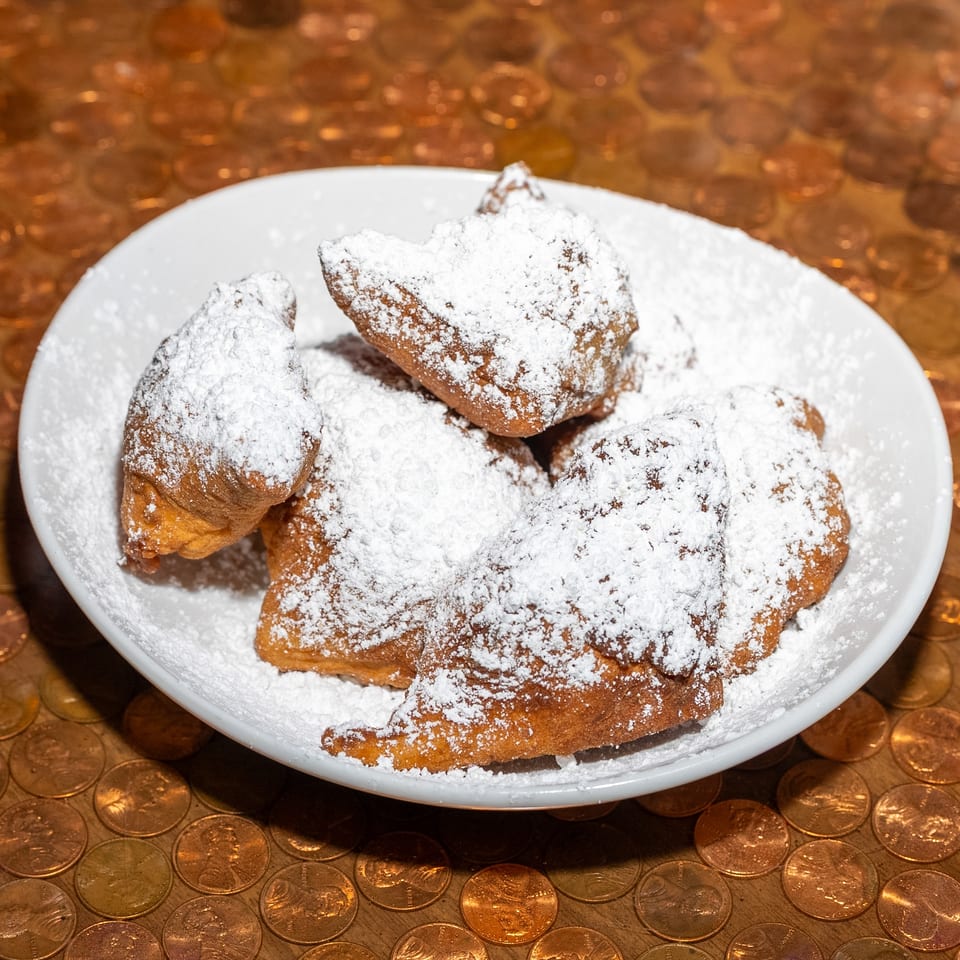 Plate of golden fried pastries generously dusted with powdered sugar on a tabletop covered with coins.