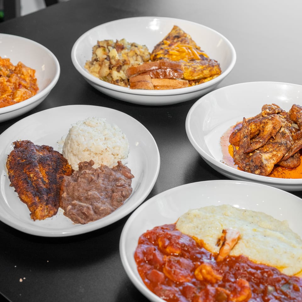 Assorted Latin American dishes arranged on white plates, including rice, beans, grilled meats, wings, plantains, and eggs.