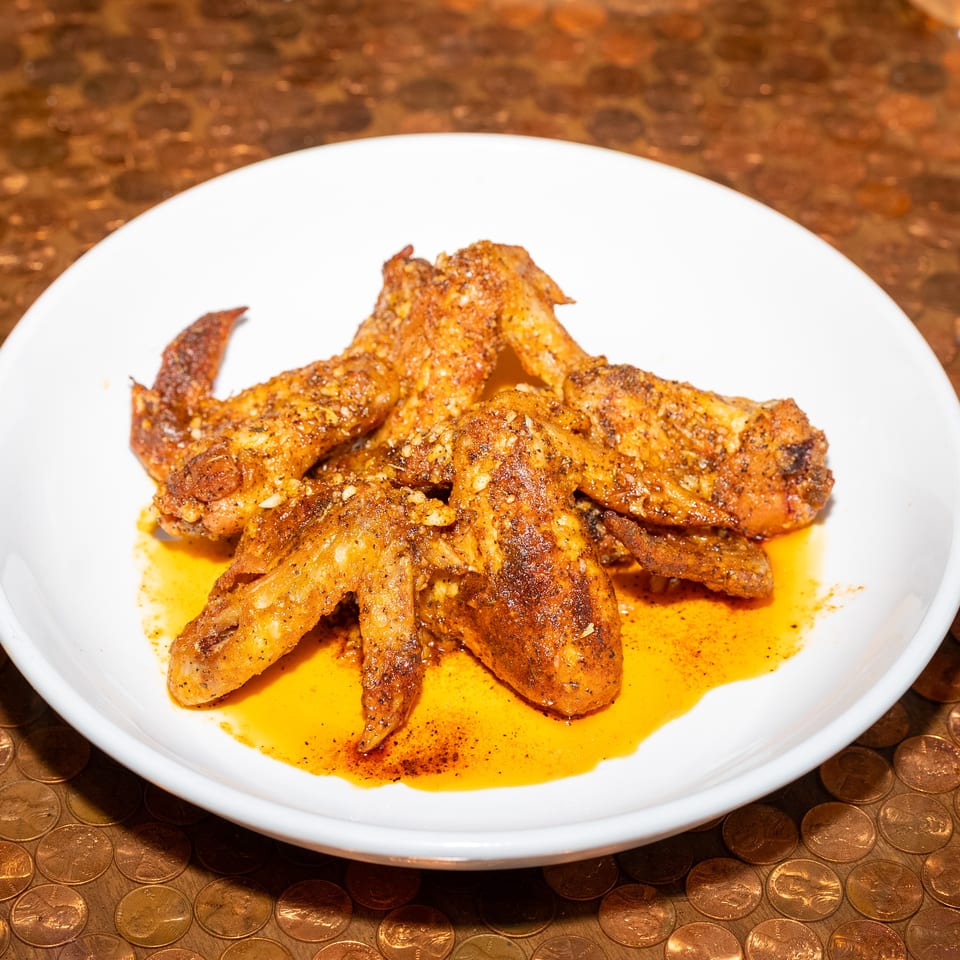 Grilled, seasoned chicken wings piled on a white plate with orange sauce, set atop a copper-colored coin-patterned table.