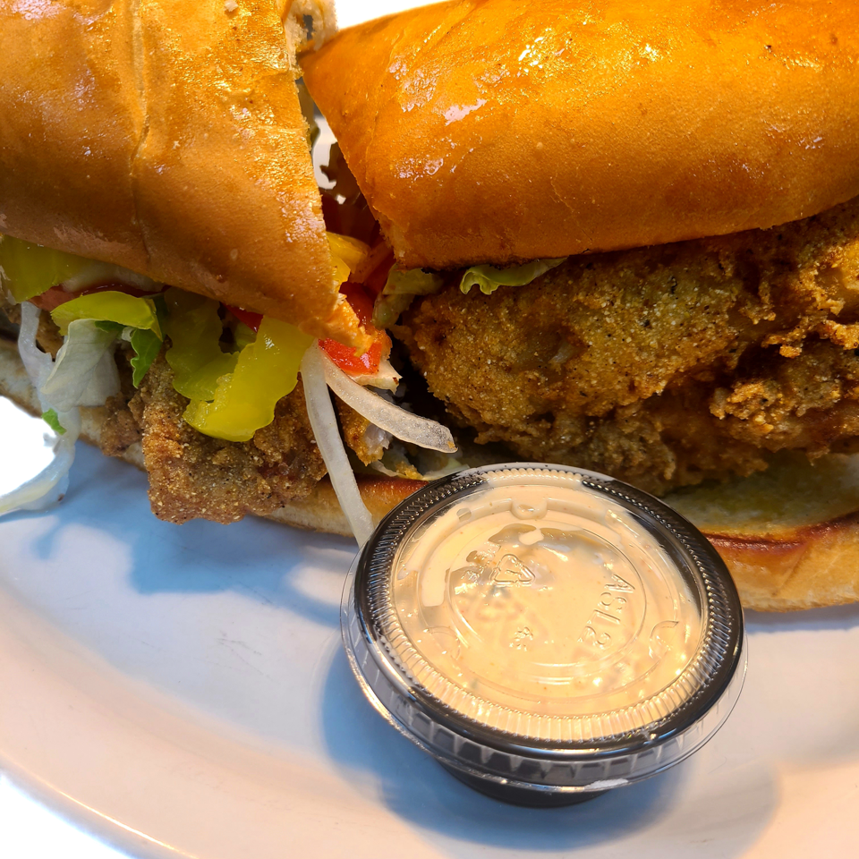 Breaded fish sandwich with lettuce, tomato, onion and dipping sauce.