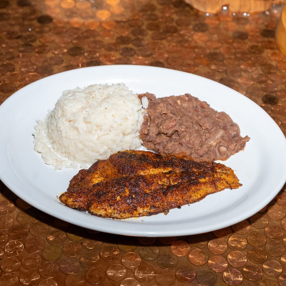 Seasoned grilled fish fillet served with white rice and refried beans on a white plate.