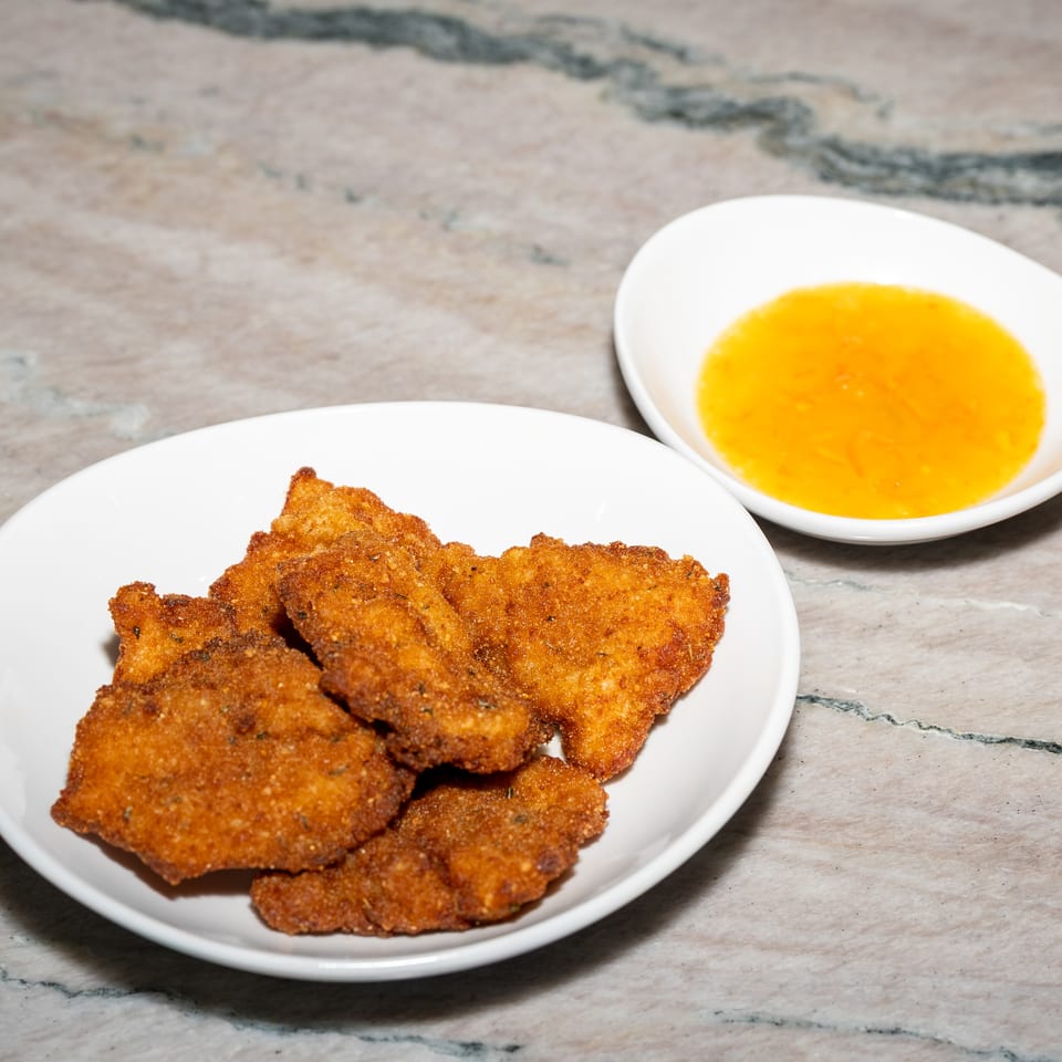 Plate of golden-brown breaded fried cutlets with a bowl of orange dipping sauce on a marble tabletop.